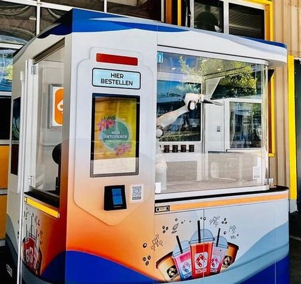 Automated drink vending machine with robotic arm inside glass enclosure.