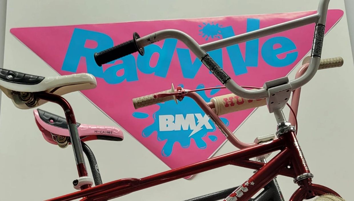 Two BMX bikes with colorful seats and handlebars in front of a vibrant Radwave BMX sign.