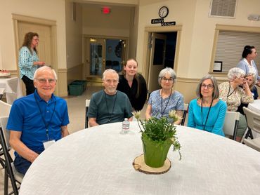 A group of five adults sitting around a round table with a green plant centerpiece.