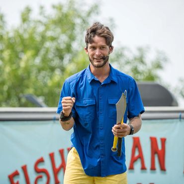 Man in blue shirt holding curved knives and wearing a headset.