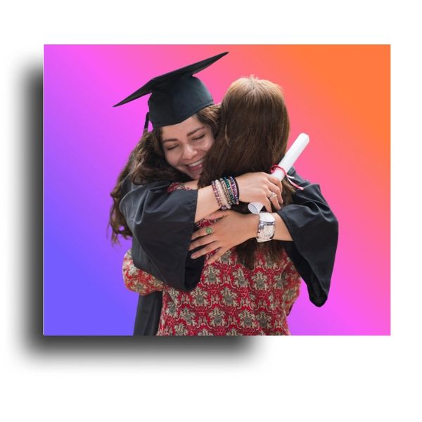 Two women embrace during a graduation celebration, one wearing a cap and gown.
