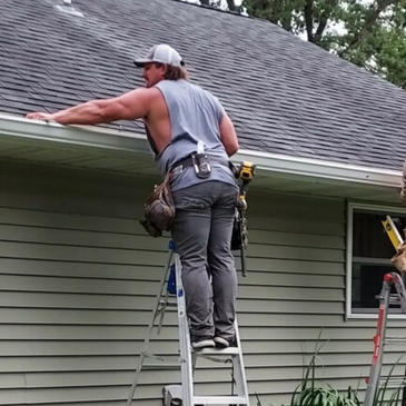 A man on a ladder working on a house gutter.
