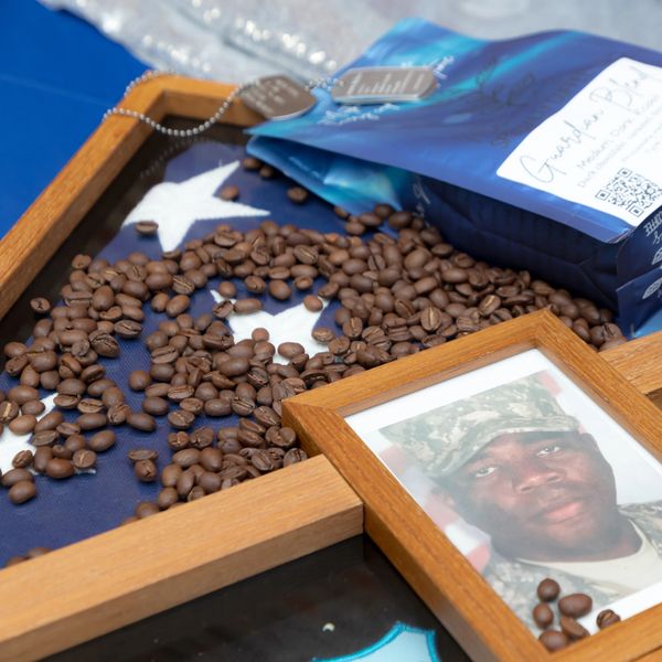 Coffee beans spilled over a folded American flag with a soldier's framed photo.