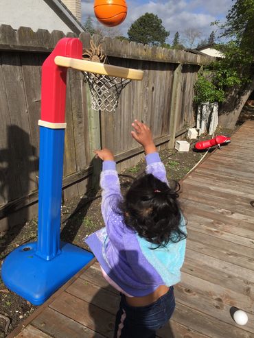 A child shoots a basketball into a small hoop outdoors.