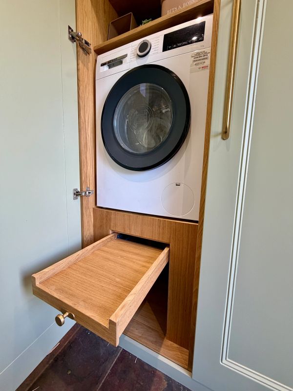 Front-loading washing machine inside wooden cabinet with pull-out drawer.