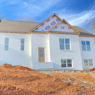 Newly constructed white brick house with exposed roof underlayment and bare ground.