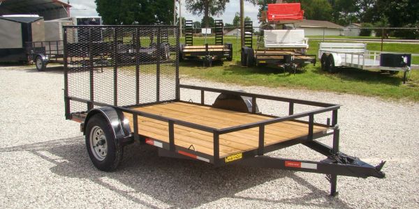 Black utility trailer with wooden floor parked on gravel.