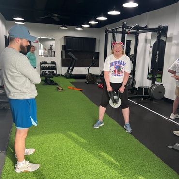 Woman lifting weights while others watch in a gym.