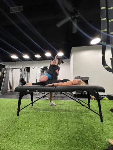 Trainer stretching a woman's leg on a massage table in a gym.