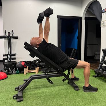 Man lifting dumbbells on an inclined bench in a gym.
