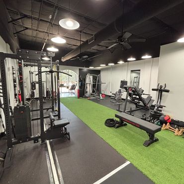 Modern gym with weight machines and green turf area under bright lights.