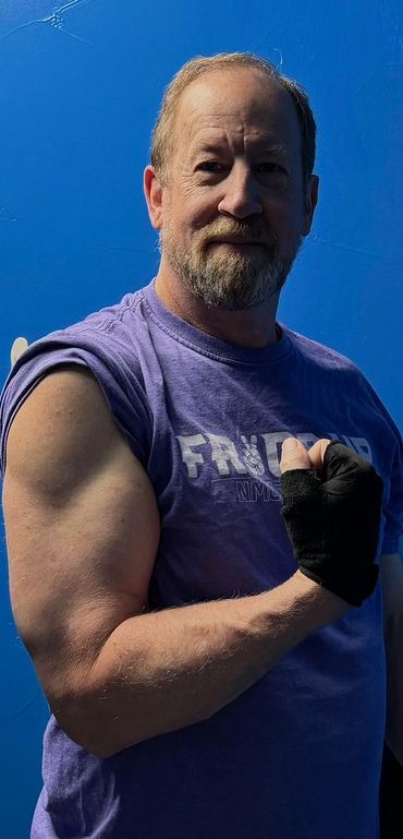 Man flexing his arm and wearing fingerless gloves against a blue wall.