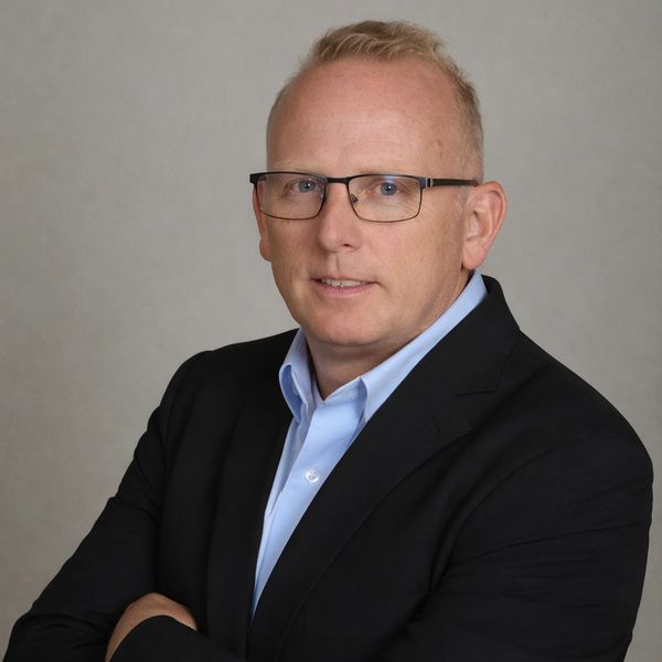 Professional man with glasses and suit posing against neutral background.