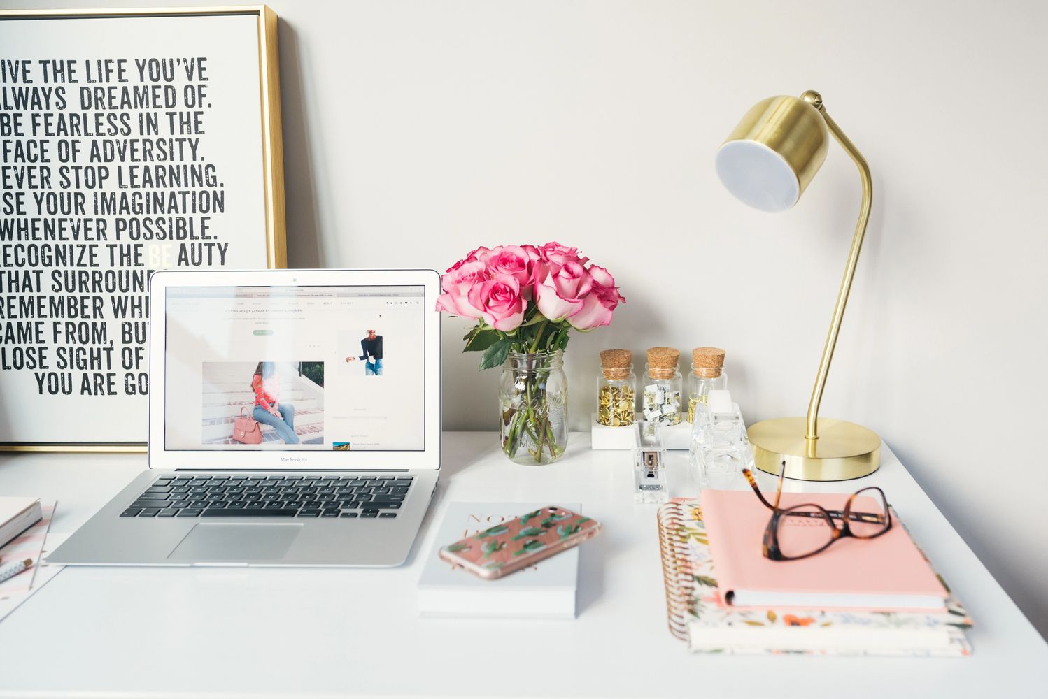 Woman's desk with table lamp, laptop computer, cell phone, books, eyeglasses