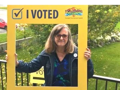 Woman holding "I Voted" frame outdoors.