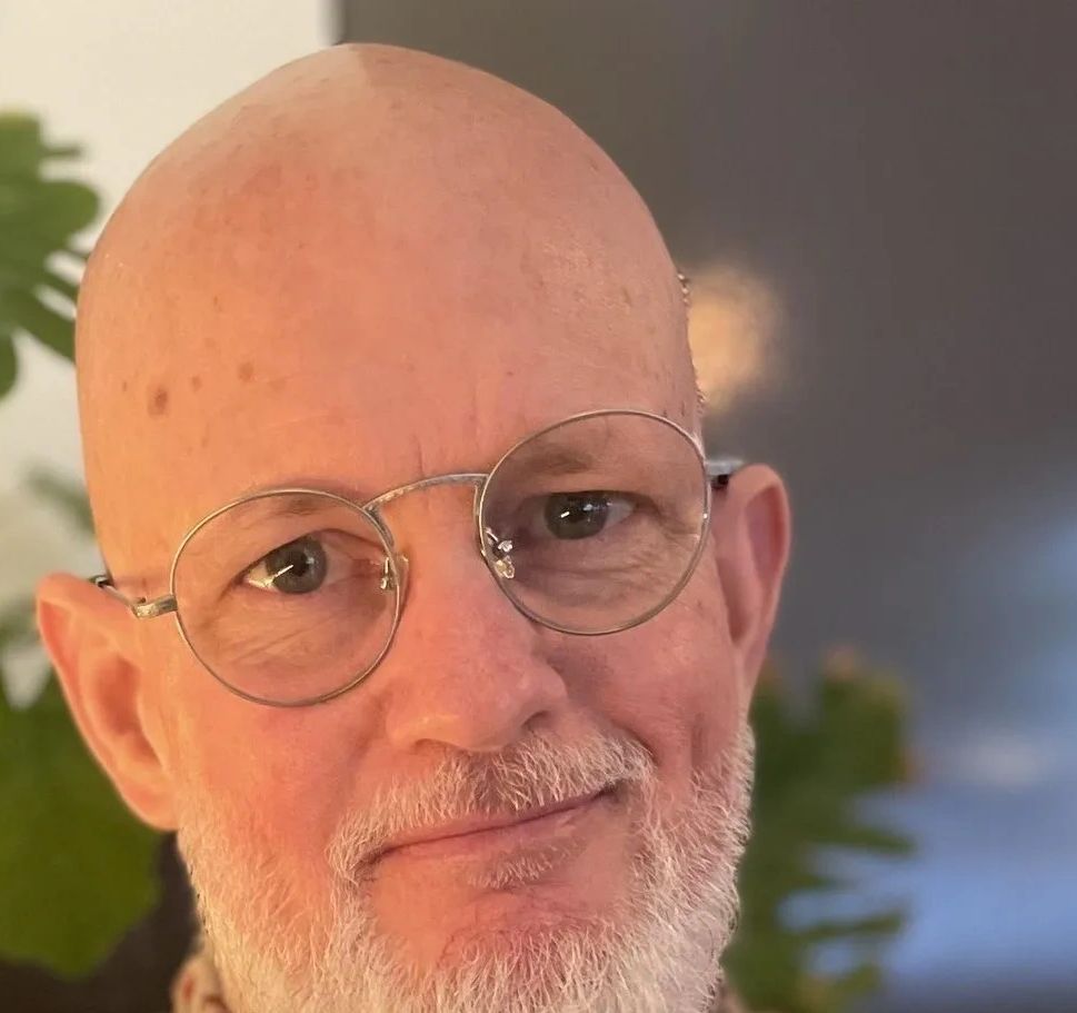 Close-up of a smiling bald man with round glasses and a white beard.
