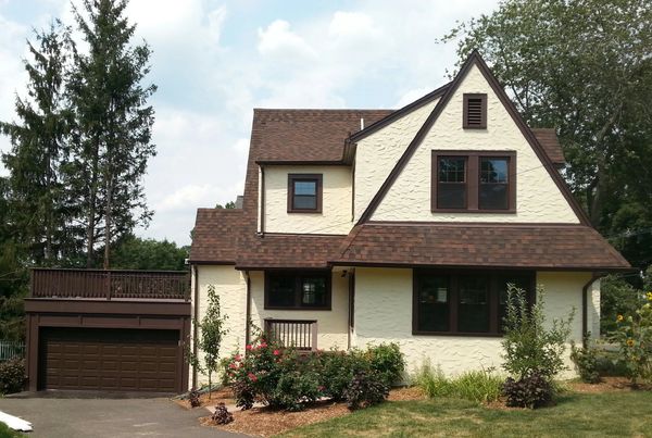 Two-story house with cream stucco walls and brown roof.