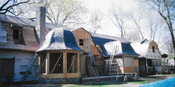 House under construction with unique curved roof sections and ladders.