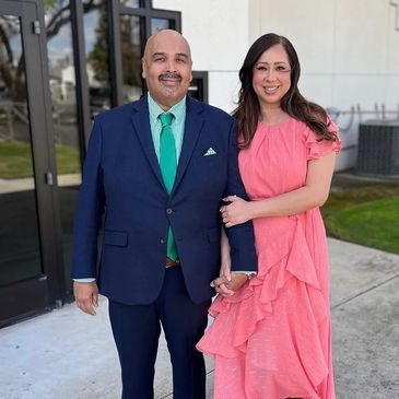 A couple dressed elegantly, smiling outdoors near a building.