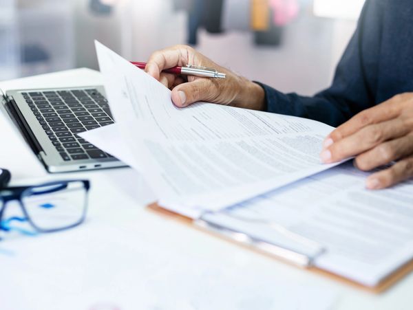 A person reviews documents at a desk with a laptop.