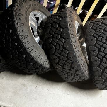 Four off-road tires with deep treads leaning against a railing.