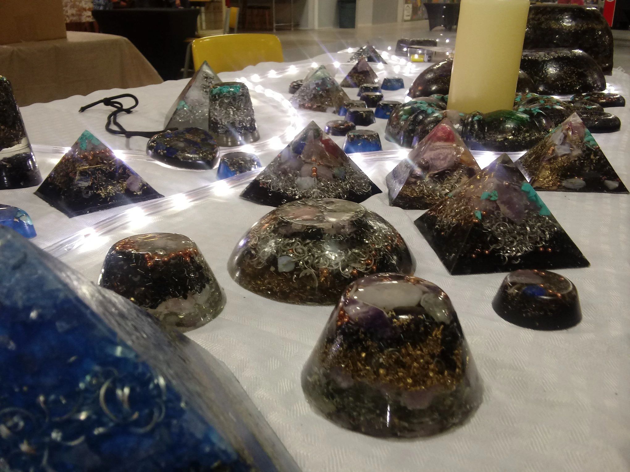 Various handmade orgonite pyramids and shapes displayed on a white cloth with lights.
