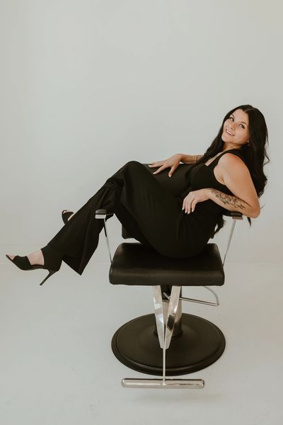 Woman in black outfit reclining on a modern black chair, smiling.