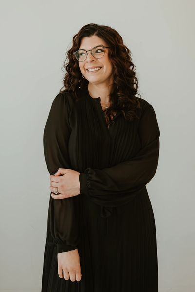 Smiling woman in black dress with glasses.
