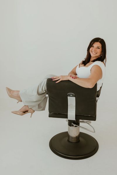 Woman sitting sideways on a black chair, smiling at the camera.