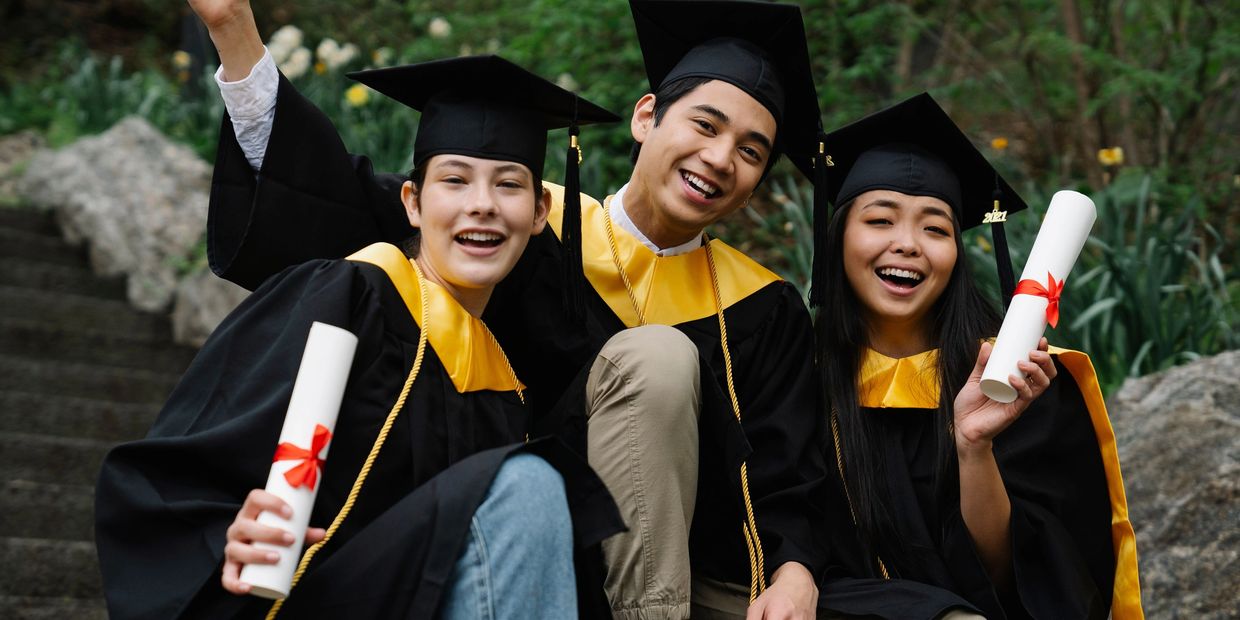 Three graduates celebrate outdoors with diplomas.