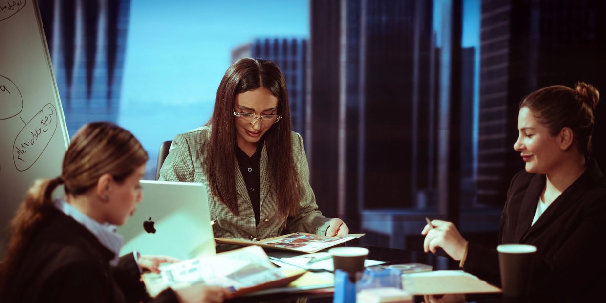 Three women working together in an office with documents and a laptop.
