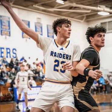 Two basketball players in action, one in white Raiders jersey, the other in black and gold.