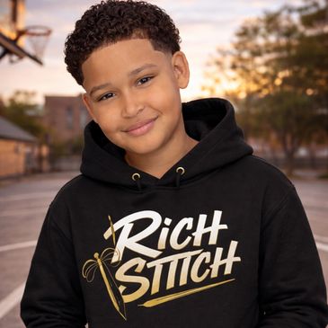 Smiling boy wearing a black hoodie with "Rich Stitch" logo outdoors at sunset.