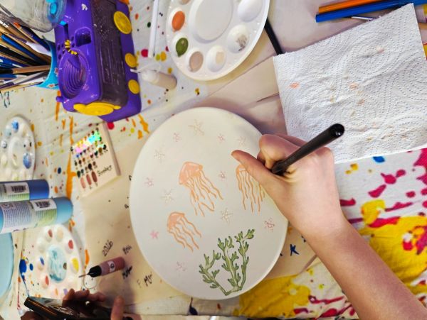 Person painting sea creatures on a white ceramic plate.