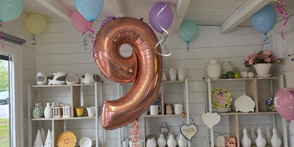 Rose gold balloon shaped as number 9 with pastel balloons in a pottery studio.