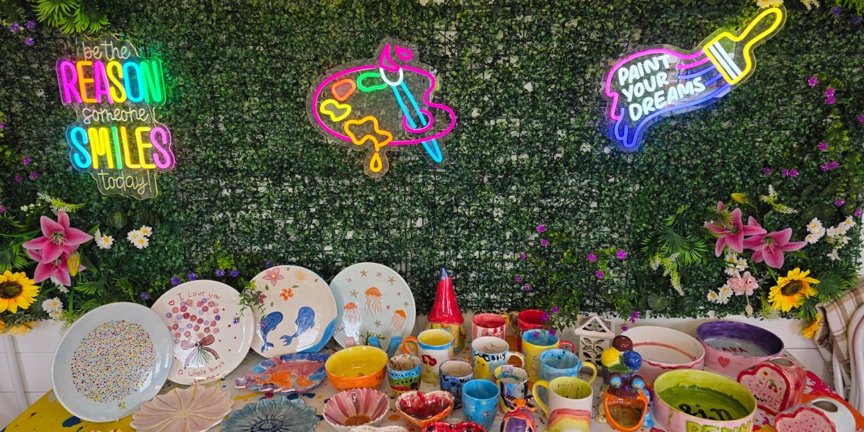 Colorful ceramic art displayed against a green floral wall with neon signs.