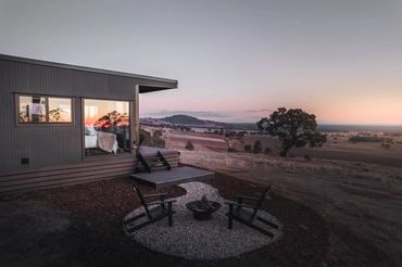 A modern cabin with a cozy fire pit overlooking a serene sunset landscape.
