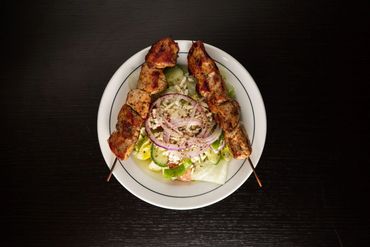 Grilled meat skewers with fresh salad on a white plate.