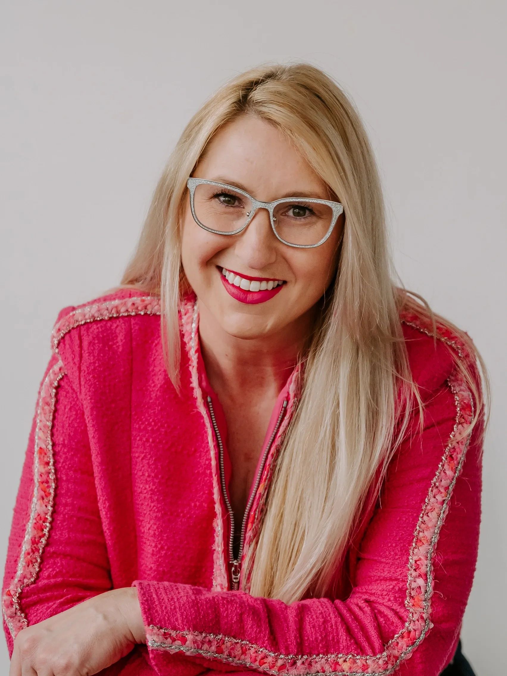 Woman with silver glasses and pink jacket, smiling