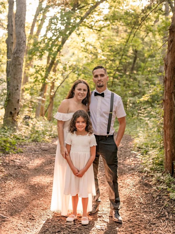 Family portrait in a sunlit forest with coordinated white outfits.