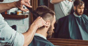 A man getting a haircut in a barbershop with a focus on the stylist's hands.