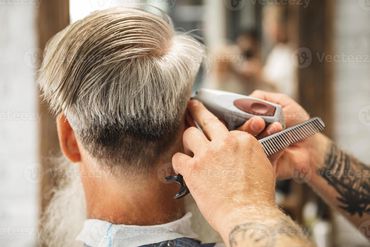 Barber trimming grey hair with clippers and comb in a salon.