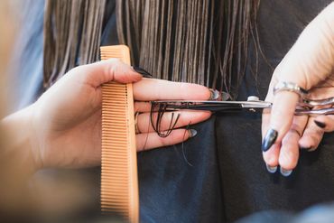 Close-up of a hairdresser cutting wet hair with scissors and a comb.