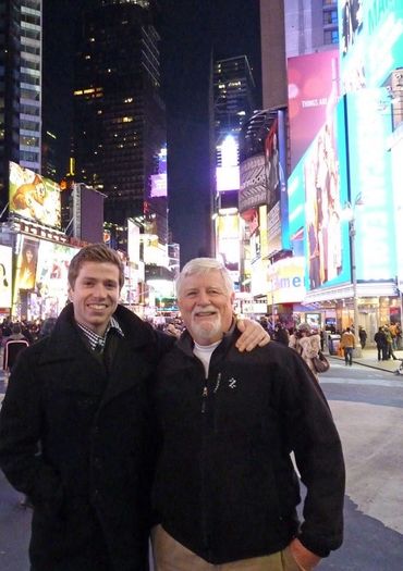 two men posing for a photo with lit city behind them