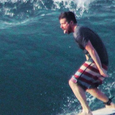 man surfing wearing black shirt and red and white shorts