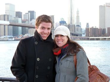 couple posing in front of water with city skyline