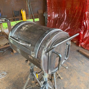 Metal furnace or forge setup on adjustable stands in a workshop.
