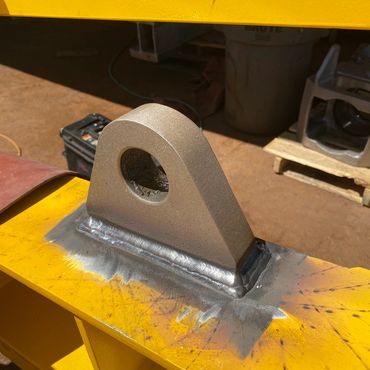 Close-up of a welded metal eyelet on yellow industrial equipment.