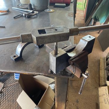 A metal tap wrench tightening a tap in a workbench vise.