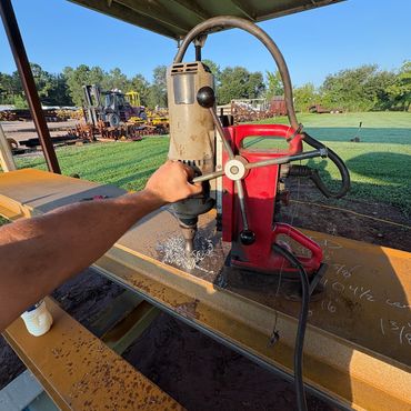 Person operating a drill press on a metal beam outdoors.